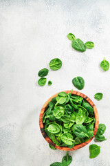 Fresh green baby spinach leaves in bowl on gray stone table background. Top view, copy space