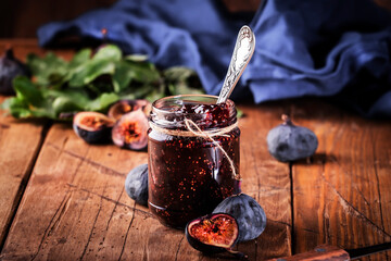 Red fig jam in jar with fresh blue figs. Homemade preparations and canning. Rustic wooden table background