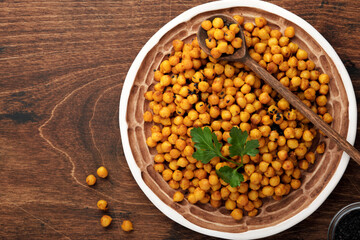 Fried chickpeas with turmeric in ceramic plate on an old wooden table background. Roasted spicy chickpeas or Indian chana or chole, popular snack recipe. Top view.
