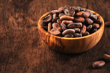 Unpeeled organic cocoa bean in bowl on wooden rustic table background. Copy space