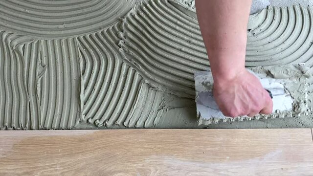 A tiler applies adhesive to the floor to install ceramic tiles. Laying tiles at a construction site. Selective focus, plenty of copy space 