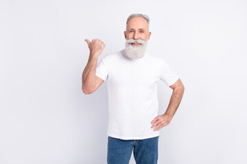Photo of cheerful grey hair beard old man point empty space wear white t-shirt jeans isolated on grey color background