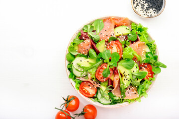 Fresh salmon salad with avocado, cucumber, sesame seeds, olive oil, tomatoes and mixed herbs. White background, top view