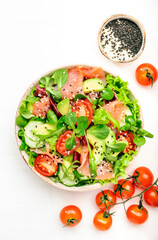 Fresh salmon salad with avocado, cucumber, sesame seeds, olive oil, tomatoes and mixed herbs. White background, top view