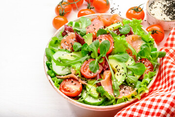 Fresh salmon salad with avocado, cucumber, sesame seeds, olive oil, tomatoes and mixed herbs. White background, top view