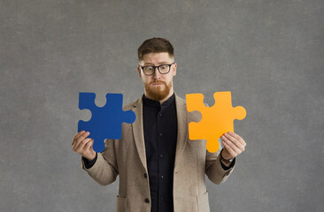 Confused man trying to solve a business problem. Young guy in hipster glasses holding two orange...