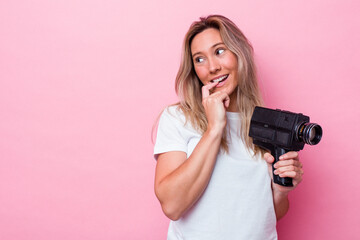 Young australian woman filming with a vintage video camera isolated relaxed thinking about...