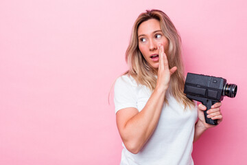Young australian woman filming with a vintage video camera isolated is saying a secret hot braking...