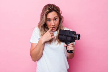 Young australian woman filming with a vintage video camera isolated biting fingernails, nervous and...