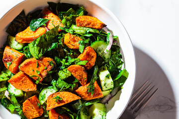 Baked sweet potato with green salad in a white bowl. Vegan food concept.