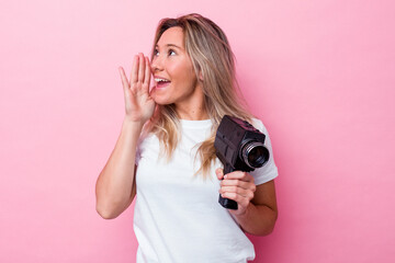 Young australian woman filming with a vintage video camera isolated shouting and holding palm near...