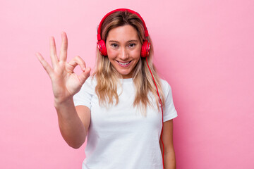 Obraz na płótnie Canvas Young australian woman listening music isolated on pink background cheerful and confident showing ok gesture.