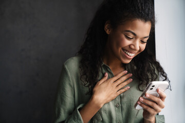 Black young woman laughing while using mobile phone indoors