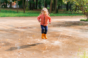 child jumping and playing in a puddle after rain, girl in the air, splashing