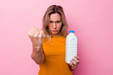 Young australian woman holding a bottle of milk isolated on pink background showing fist to camera, aggressive facial expression.