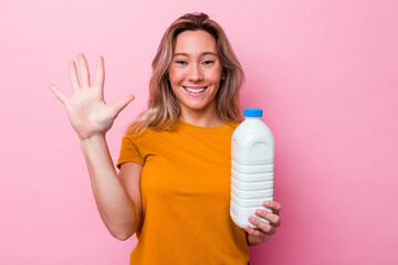 Young australian woman holding a bottle of milk isolated on pink background smiling cheerful showing number five with fingers.