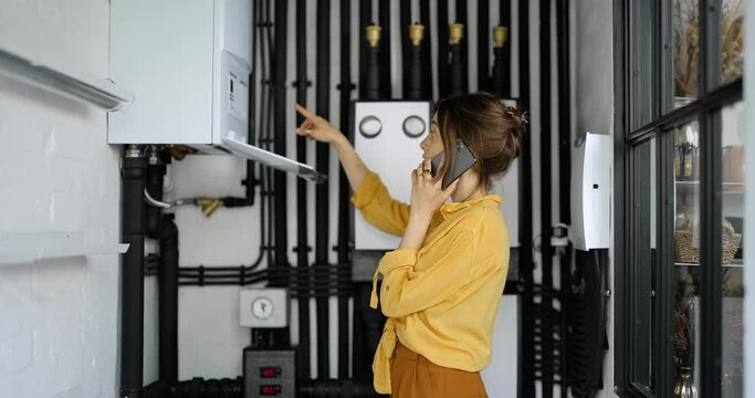 Confused woman having problems with heating system at home, speaks on the phone trying to solve the problem. Concept of female incompetence in home appliances