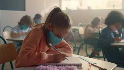 Smart girl in medical mask schooling in classroom during coronavirus pandemic