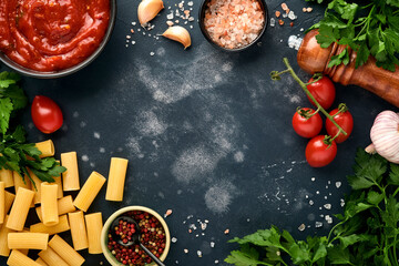 Pasta background. Pasta rigatoni, tomato ketchup sauce, olive oil, spices, parsley, and fresh tomatoes on a dark slate, stone or concrete background. Top view with copy space.