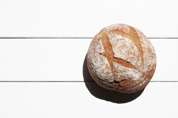 Sourdough bread, tasty round dark bread in the sunlight, placed on a wooden white table. At the left copy space for your own text.