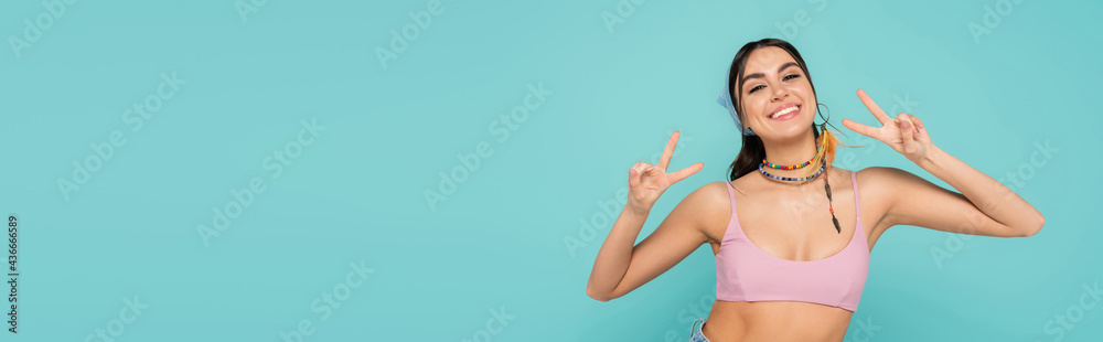 Wall mural smiling woman in top showing victory gesture isolated on blue, banner.