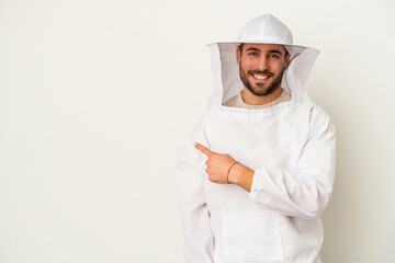 Young apiculture caucasian man isolated on white background smiling and pointing aside, showing something at blank space. - obrazy, fototapety, plakaty