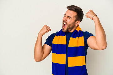 Young caucasian fan of a soccer team isolated on white background raising fist after a victory,...