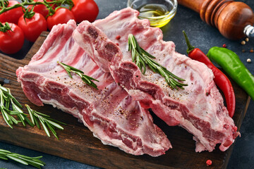 Raw pork ribs or fresh uncooked meat with spices on black wooden tray with paprika, garlic cloves and herbs. Dark textured background with copy space for text.