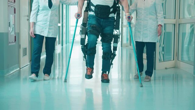 A man in the exoskeleton is walking with doctors' help