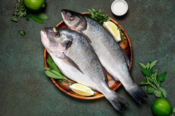 Uncooked fish with lime and herbs in a wooden bowl on a dark green background top view. Raw dorada and seabass.