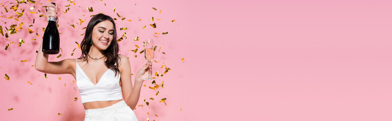 Stylish woman with champagne near festive confetti on pink background, banner.