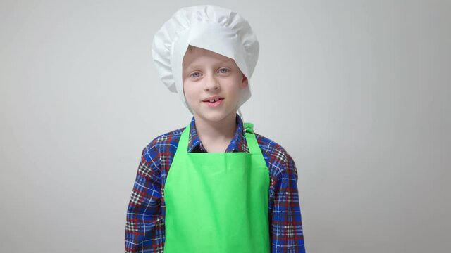 little cook boy in green apron and chef's hat stands and shows sign of belissimo idea of cooking new dish hobby schoolboy in cook's costume kitchen food restaurants public catering cooking food