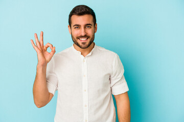 Young caucasian man isolated on blue background cheerful and confident showing ok gesture.