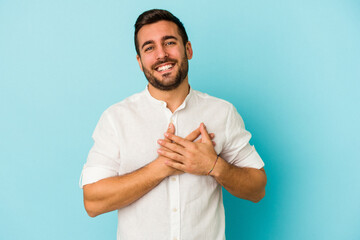 Young caucasian man isolated on blue background laughing keeping hands on heart, concept of happiness.