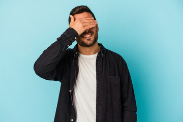 Young caucasian man isolated on blue background covers eyes with hands, smiles broadly waiting for a surprise.