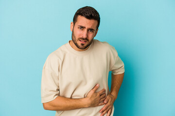 Young caucasian man isolated on blue background having a liver pain, stomach ache.