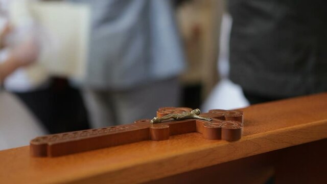 A wooden cross with a crucifix lies in the church, with parishioners walking in the background. Church utensils.
