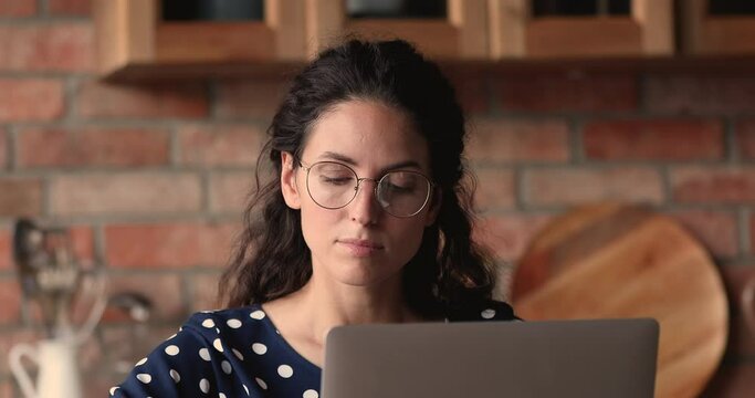 Close up head shot focused young pretty latin woman in eyeglasses working distantly on computer, considering tasks or problems solution, web surfing information online or studying alone at home.