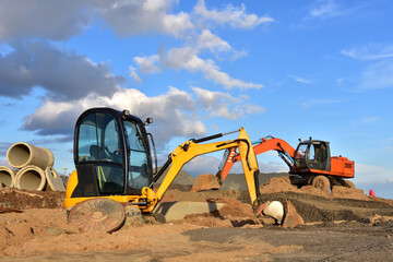 Mini excavator during earthmoving at construction site. Backhoe dig ground for the construction of foundation and laying sewer pipes district heating. Earth-moving heavy equipment on road works