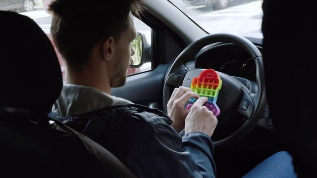 Caucasian man sits behind the steering wheel in car and presses bubbles in anti stress toy. Man is resting and relaxing, resting in the car 
