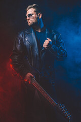 Brutal bearded Heavy metal musician in leather jacket, cap and sunglasses is playing electrical...