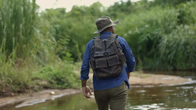 Hiker man crossing the river and looking at beautiful forest. Hiker man hiking in forest with a backpack. Male model outdoors in nature.