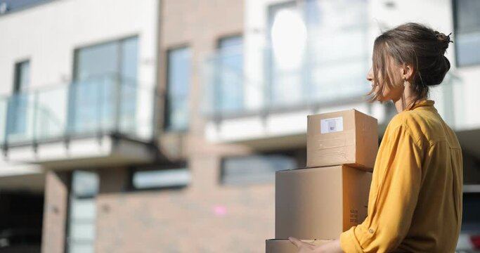Young happy woman carries home a parcels with goods purchased online at the modern residential district. Concept of online shopping and delivery