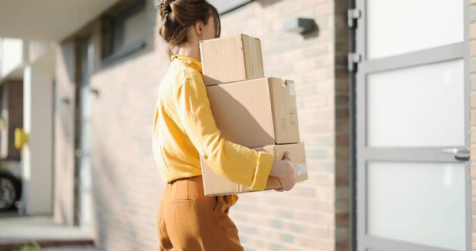 Young happy woman carries home a parcels with goods purchased online, knocking on the door. Concept of online shopping and delivery