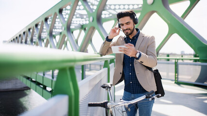 Young business man commuter with bicycle going to work outdoors in city, video call on smartphone.