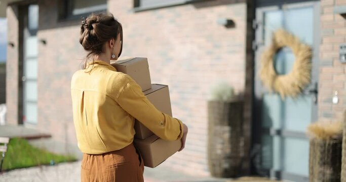 Young happy woman carries parcels with goods purchased online, opening the door and going home. Concept of online shopping and delivery