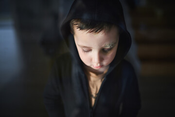 Close-up of sad small boy with cut eyebrow standing indoors at home, poverty concept.