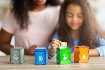 Eco-friendly family activities. Lovely little black girl with her mother playing garbage sorting board game at home
