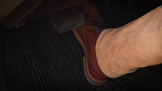 Man in brown shoes taking a leg off from brake pedal and pressing the accelerator pedal in a car. Close-up of man's boot smoothly pressing the gas pedal while driving a car