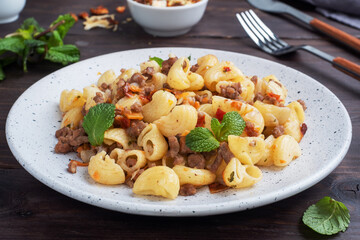 Stewed pasta with minced beef and vegetables, macaroni in Navy style on a plate. Dark wooden background.